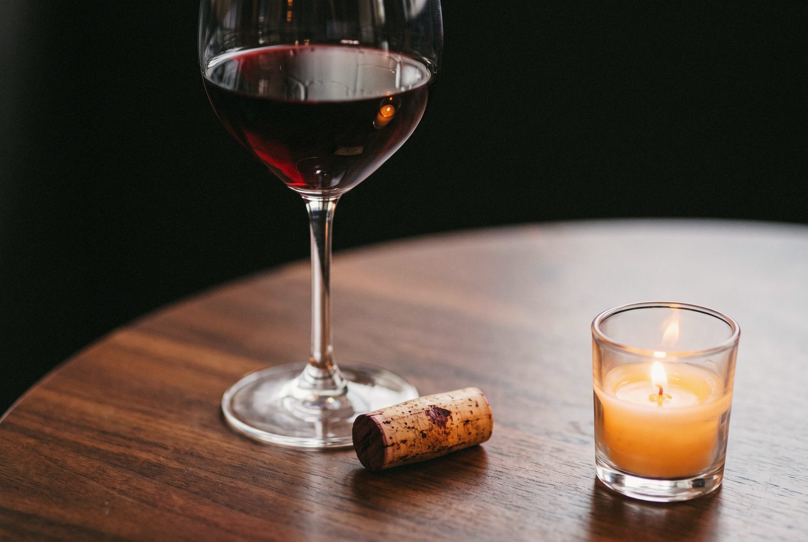 A glass of red wine and a cork by candlelight